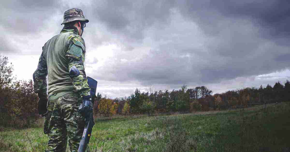 An image of a hunter wearing a hunting camo and carrying a riffle in an open field