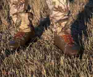 An image of a pair of boots for hunting worn by a camouflaged hunter 